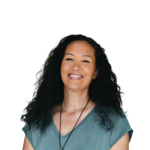 Portret foto van coach Pamela waar ze lachend op staat in een turquoise shirt en met een witte achtergrond.