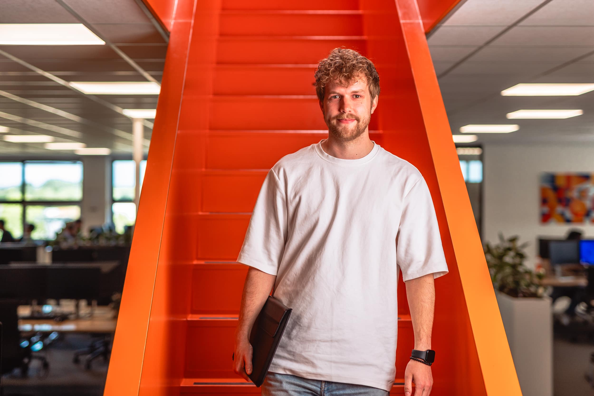 Collega komt naar beneden lopen van oranje trap in kantoorpand.