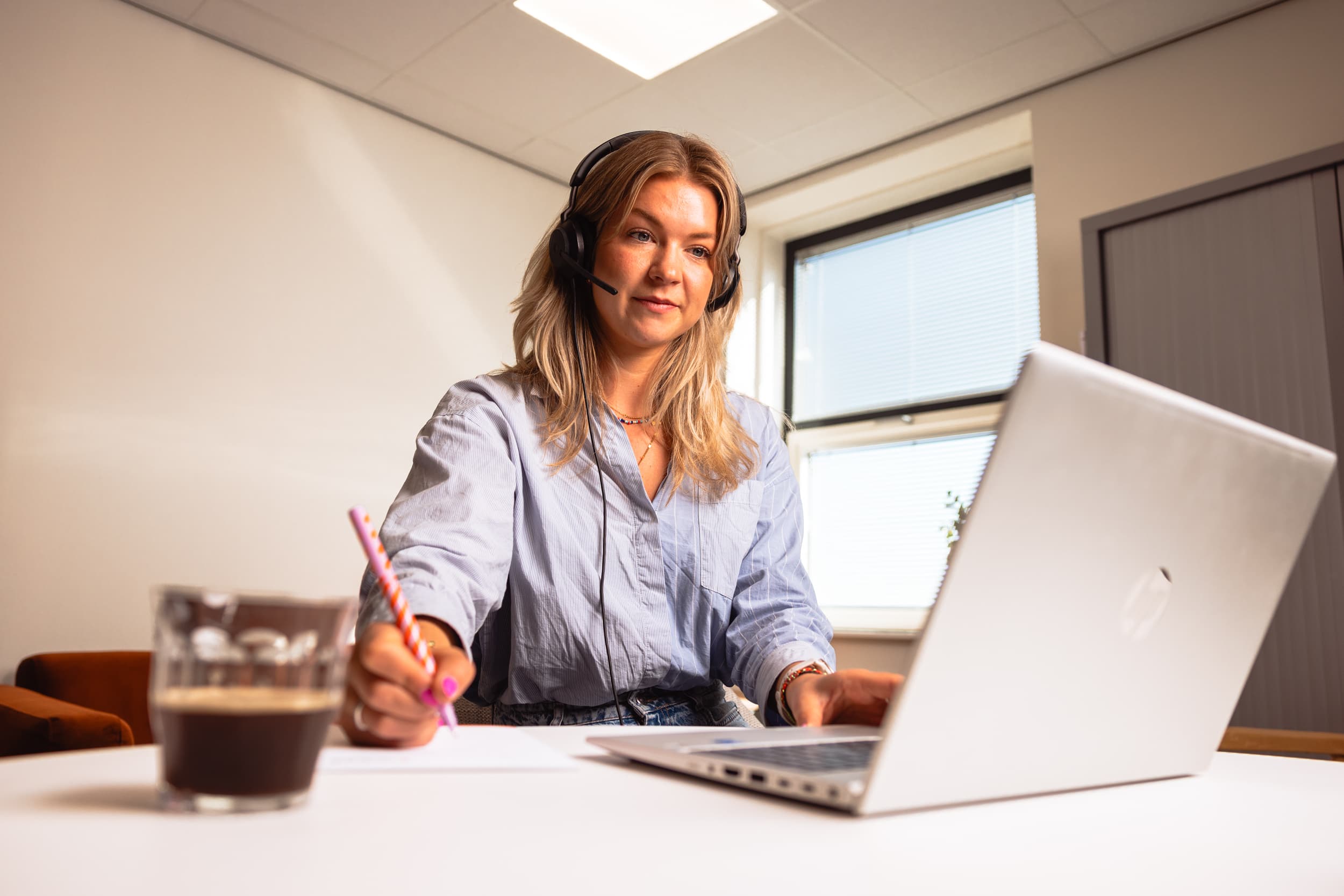 Collega belt met een headset en heeft een kop koffie.