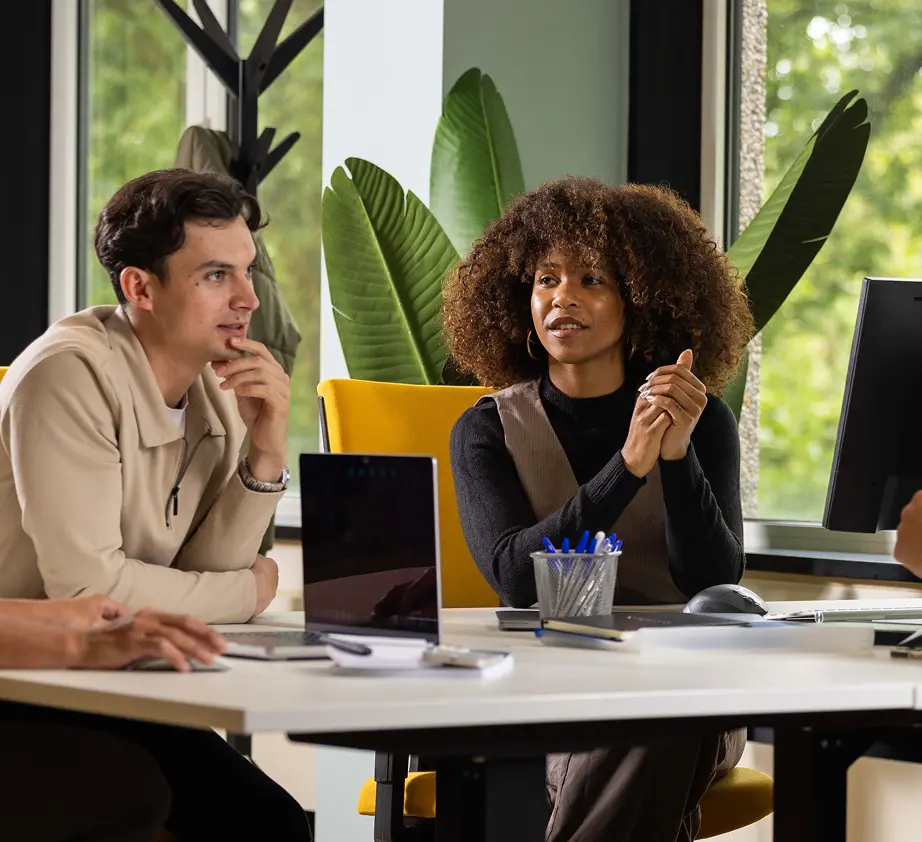 Drie collega's in vergadering aan een bureau waarbij een dame en een heer met elkaar aan het spreken zijn