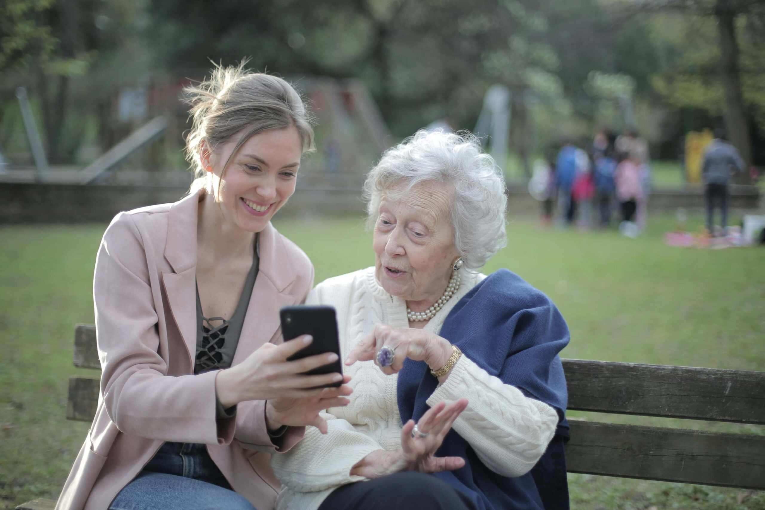 Jongere vrouw zit in park met een vrouw op leeftijd en laat haar wat zien. ze lachen samen.